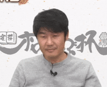 a man wearing a gray shirt has a microphone attached to his neck in front of chinese writing