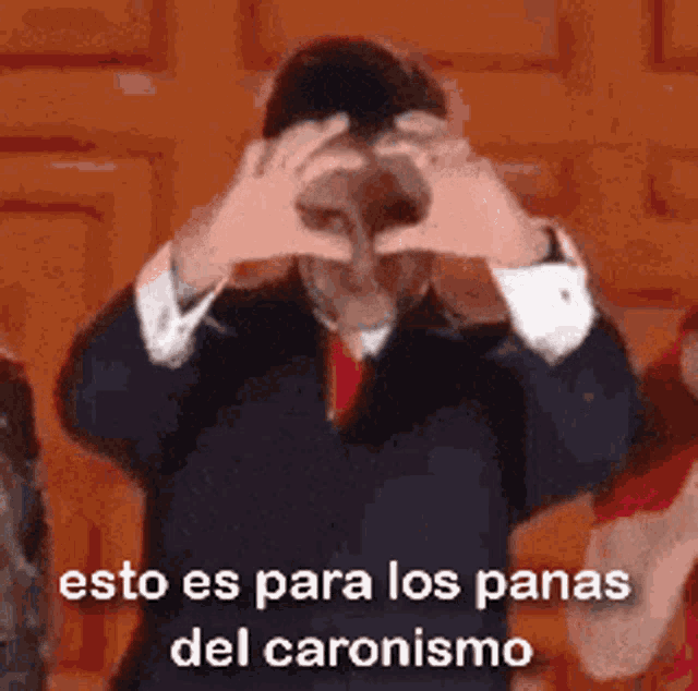 a man in a suit is making a heart shape with his hands .