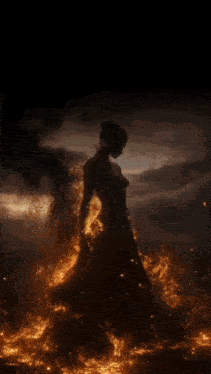 a woman in a long dress is surrounded by flames and smoke .