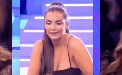 a woman in a black dress is sitting in front of a blue screen and crying .