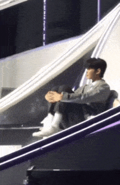 a man is sitting on a stage with his legs crossed and his hands folded .
