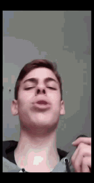 a young man is making a funny face with his eyes closed while holding something in his hand .