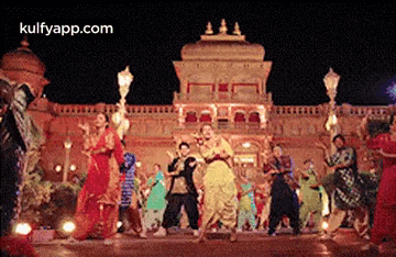 a group of people are dancing in front of a building with the website kulfyapp.com in the corner .