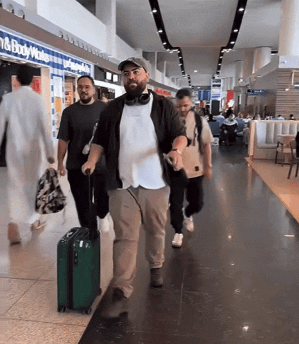a group of men are walking through an airport with a sign that says bath & body works