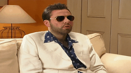 a man sitting on a couch wearing sunglasses and a white jacket
