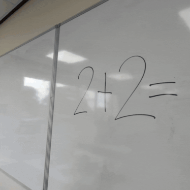 a man is writing on a white board with a marker and the number 2 is written on it