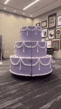 a large purple cake with white frosting is in a room with pictures on the wall