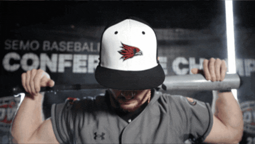 a man holding a bat in front of a semo baseball conference sign
