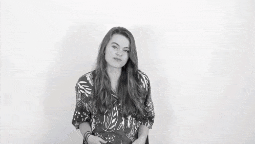 a woman in a blue shirt is standing in front of a white wall and making a funny face .