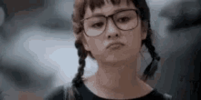 a close up of a woman wearing glasses and pigtails making a sad face .
