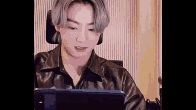 a young man with gray hair is sitting in a chair looking at a tablet .