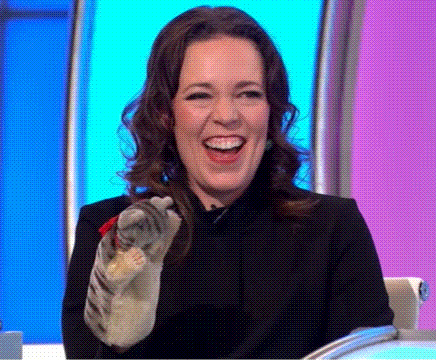 a woman is laughing while holding a cat in her hand on a television show .