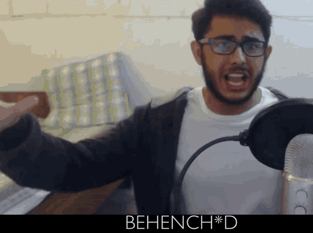 a man with glasses and a beard is standing in front of a microphone with the words behench * d written below him