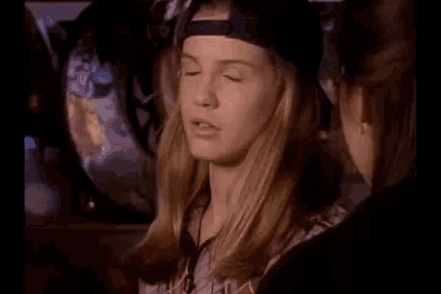 a young woman wearing a baseball cap and a plaid shirt is talking to another woman .