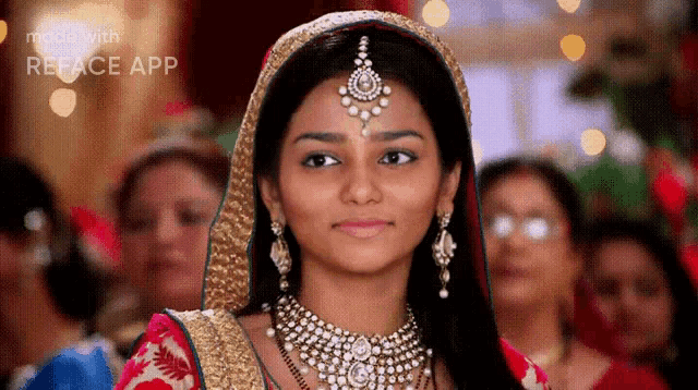 a woman wearing a veil and jewelry is smiling in front of a crowd of people .