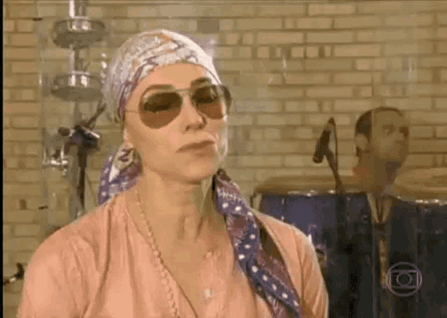a woman wearing sunglasses and a head scarf is standing in front of a microphone .