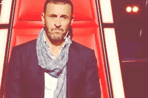a man with a scarf around his neck is sitting in a red chair