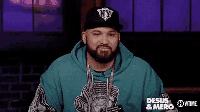 a man with a beard wearing a hat and a blue hoodie is making a funny face .
