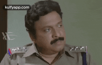 a man with a mustache is wearing a police uniform and looking at the camera .