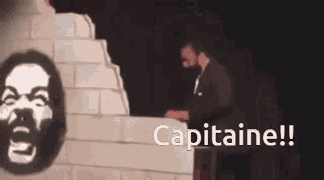 a man in a suit stands in front of a brick wall with the words capitaine written on the bottom