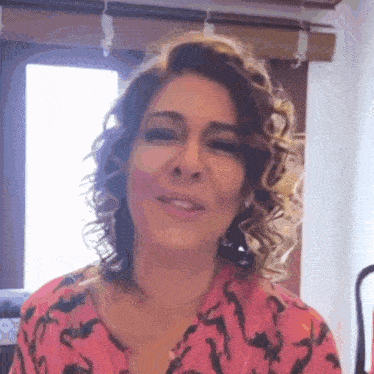 a woman with curly hair is wearing a pink shirt and earrings .