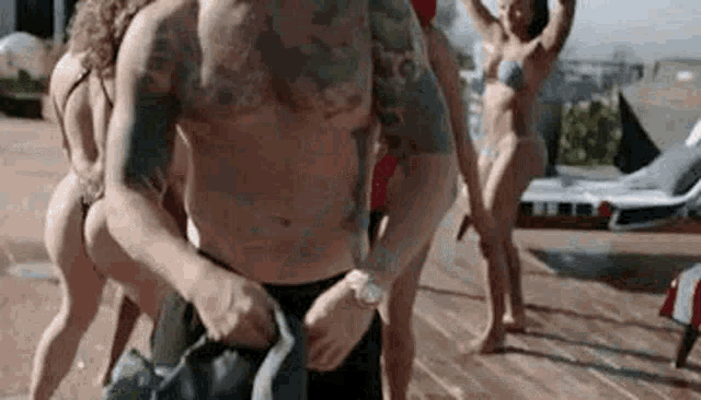 a group of people in bikinis are standing around a man in a shirtless photo .
