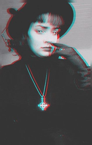 a woman wearing a hat and a cross necklace looks at the camera