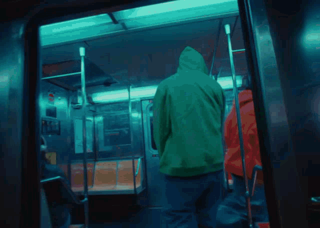 a man in a green hoodie is standing on a train