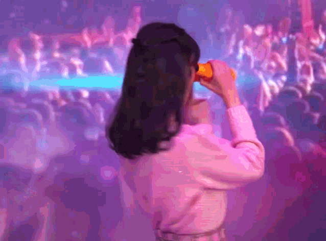 a woman in a pink shirt looks through binoculars at a crowd of people