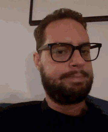 a man with a beard wearing glasses looks at the camera