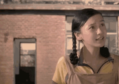 a young woman with pigtails is standing in front of a brick building and looking at the camera .
