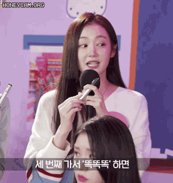 a woman is holding a microphone in front of another woman with korean writing on it