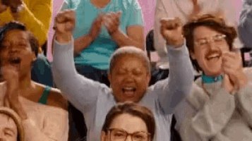 a group of people are sitting in a stadium with their arms in the air and clapping .