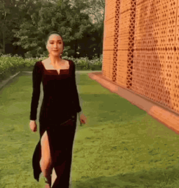 a woman in a black dress is walking in front of a brick wall