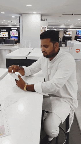 a man in a white shirt sits at a table in front of a sony display