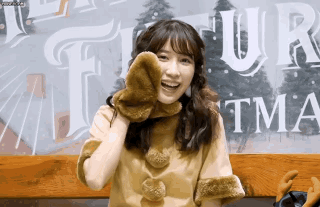 a woman wearing a fur coat and mittens is smiling in front of a sign that says fur tma