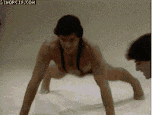 a woman in a bikini is doing push ups while a man looks on
