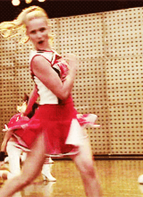 a cheerleader in a red and white outfit is dancing on the floor