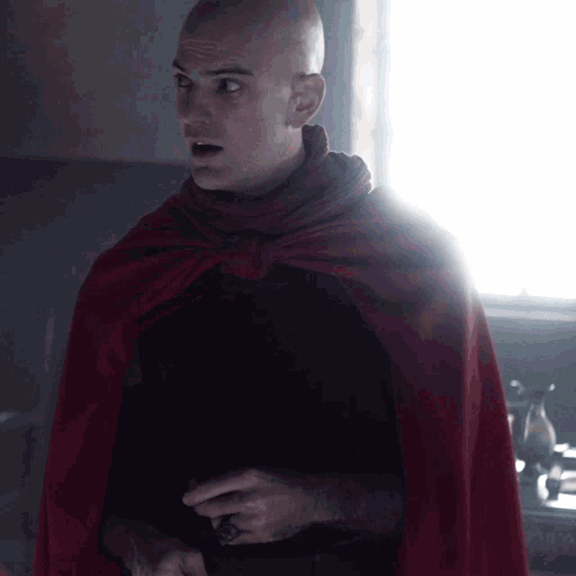 a bald man wearing a red cape and black shirt