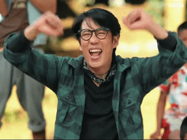a man wearing glasses and a green plaid shirt with his arms in the air