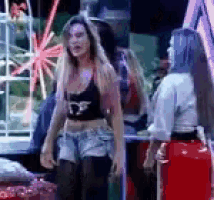 a woman in a black crop top and shorts is standing next to another woman in a red skirt .