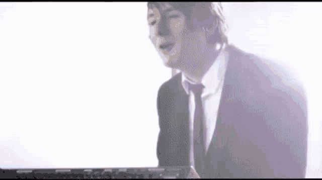 a man in a suit and tie is singing into a microphone while standing in front of a window .