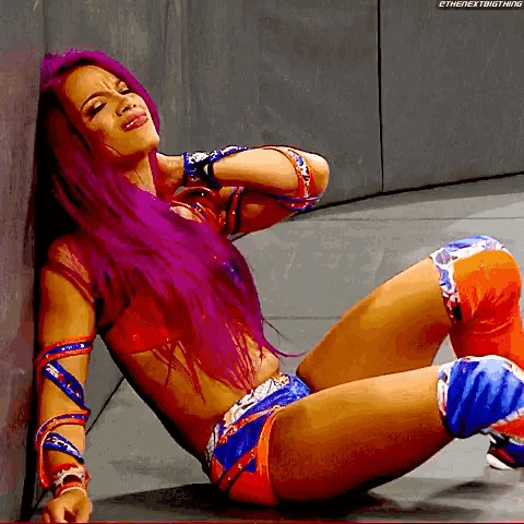 a female wrestler with purple hair is laying down on the floor .
