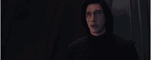 a man with long hair is standing in a dark room with a red light behind him .