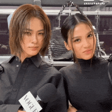 two women standing next to each other holding a vogue microphone