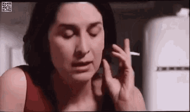 a woman is smoking a cigarette in a kitchen with her eyes closed .