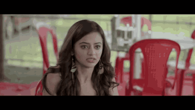 a woman is sitting at a table with red chairs in front of her