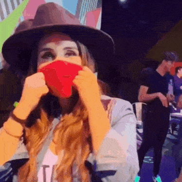 a woman wearing a hat is covering her face with a red mask .