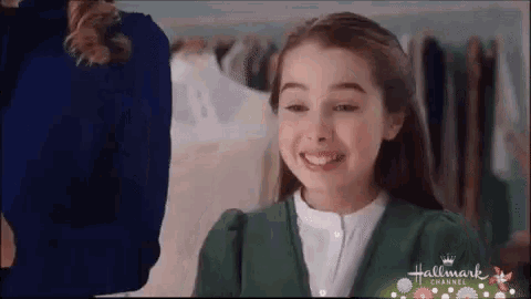 a young girl in a green sweater is smiling while standing in front of a closet .