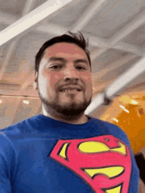 a man with a beard is wearing a superman t-shirt and smiling .